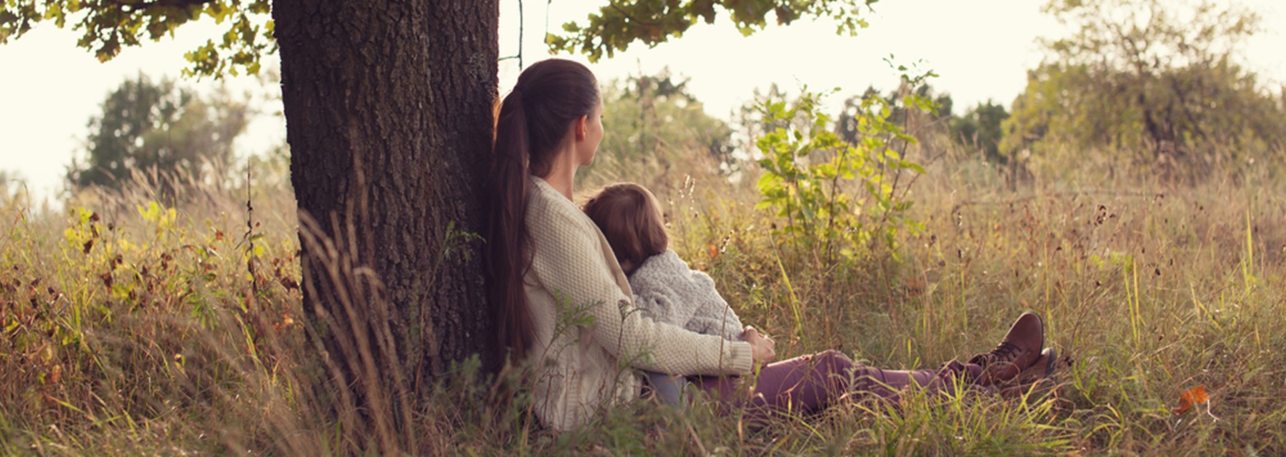 Mother sitting on ground under a tree holding a toddler