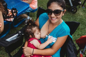 woman in sunglasses smiling at camera and nursing a toddler