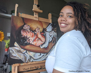 Lauren J. Turner sitting in front of one of her paintings of a baby nursing