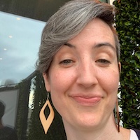 Person with short bob and large earrings is smiling at the camera.