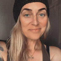 White person with long blonde hair and a beanie is smiling at the camera.
